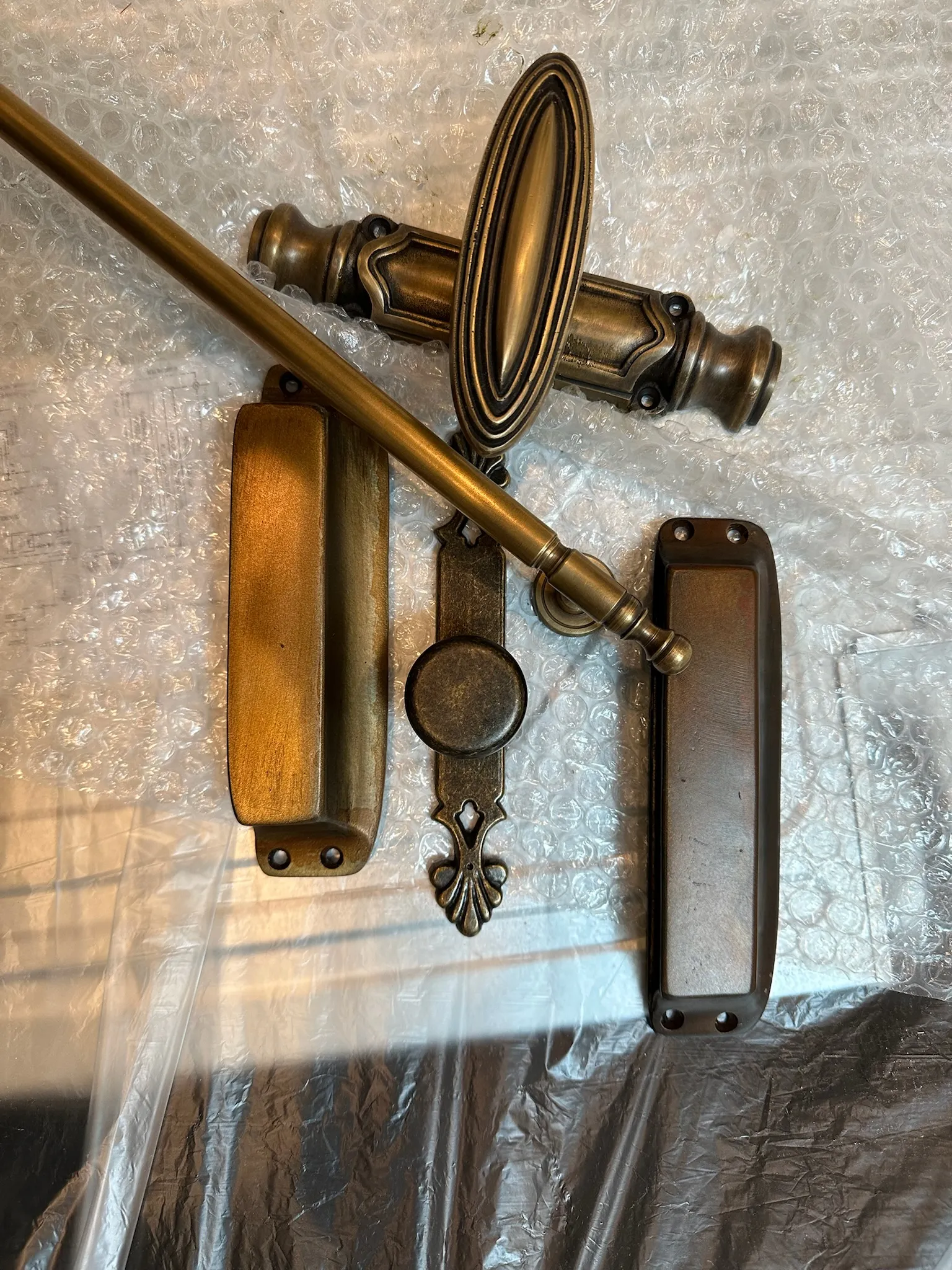 A curated collection of ornate antique brass and bronze door hardware, including handles and pulls, laid on protective bubble wrap. Ideal for classic interiors.