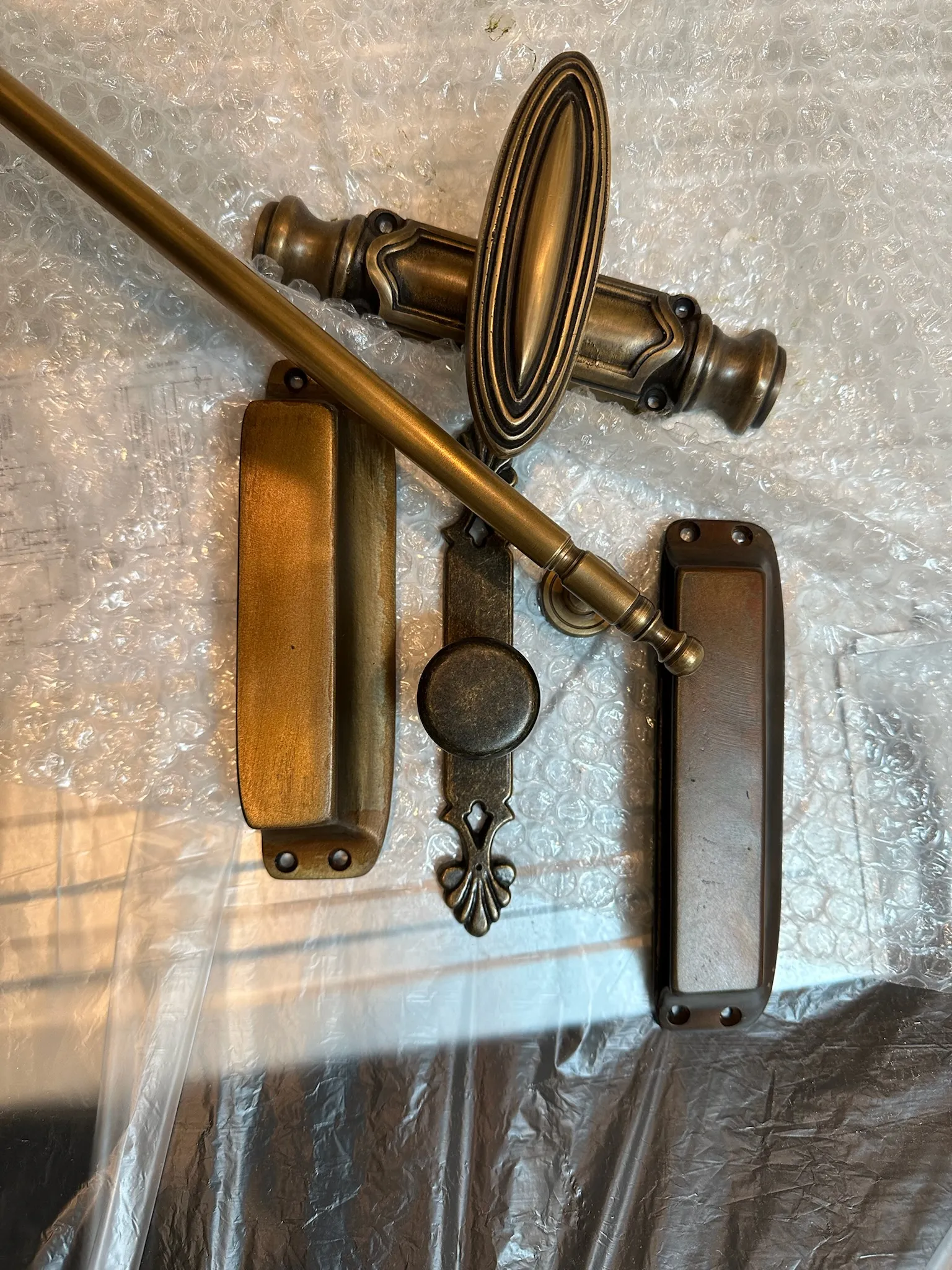 A collection of ornate antique brass and bronze decorative hardware, including door handles, pulls, and escutcheons, displayed on bubble wrap.