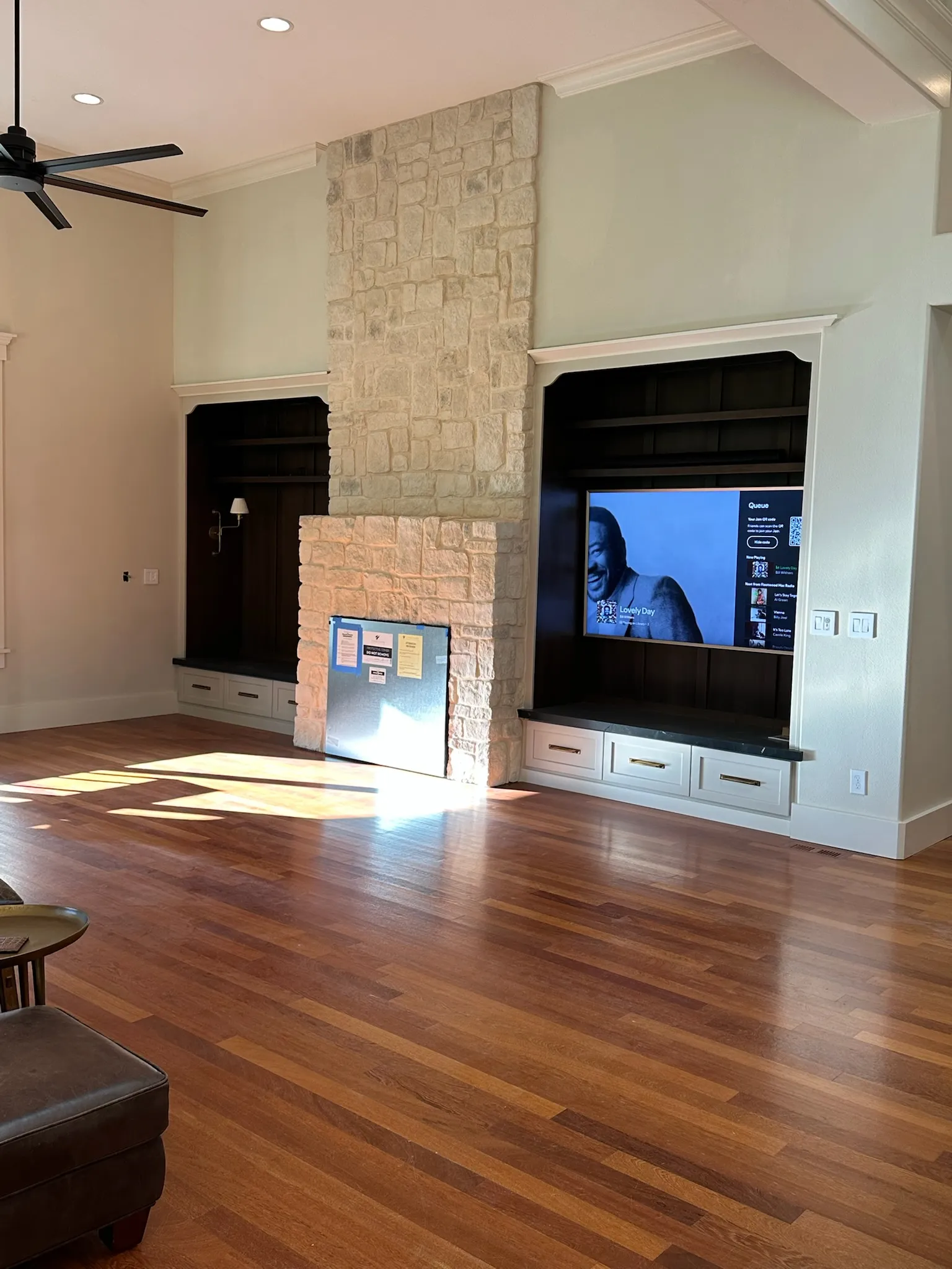 Spacious living room featuring a prominent stone fireplace flanked by custom dark wood built-in cabinetry with a TV display and storage, on rich hardwood floors.
