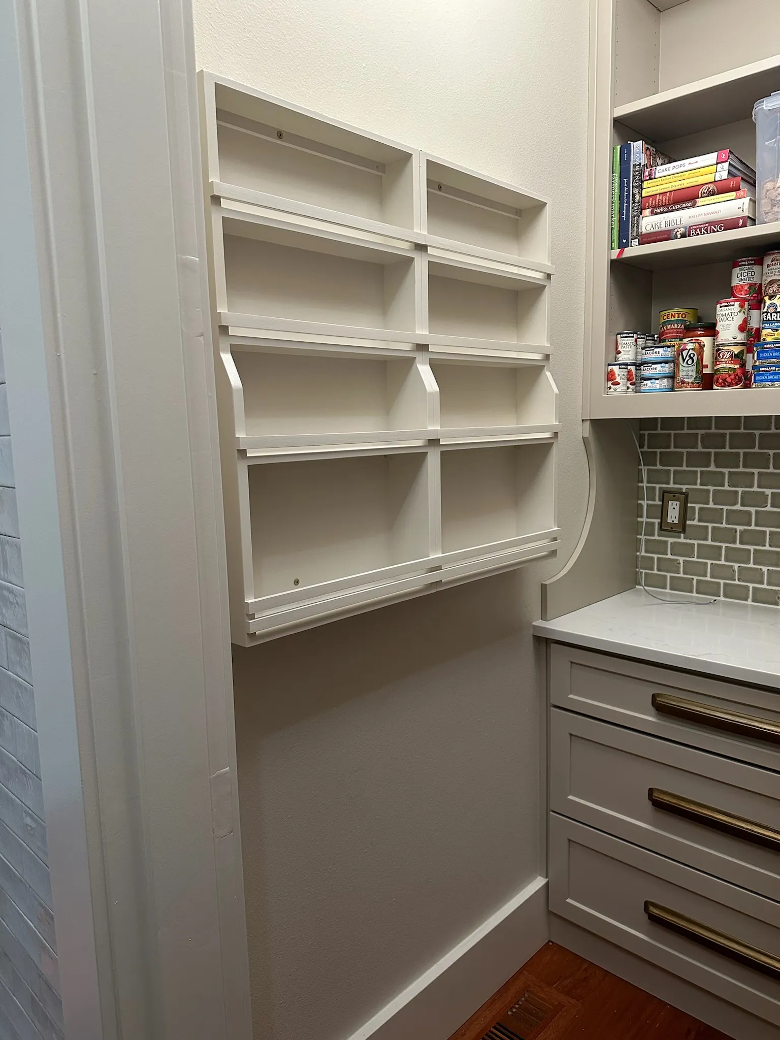 View of a well-organized transitional pantry featuring empty wall-mounted spice racks, custom cabinetry with brass hardware, and a stylish subway tile backsplash. Ideal for kitchen storage solutions.