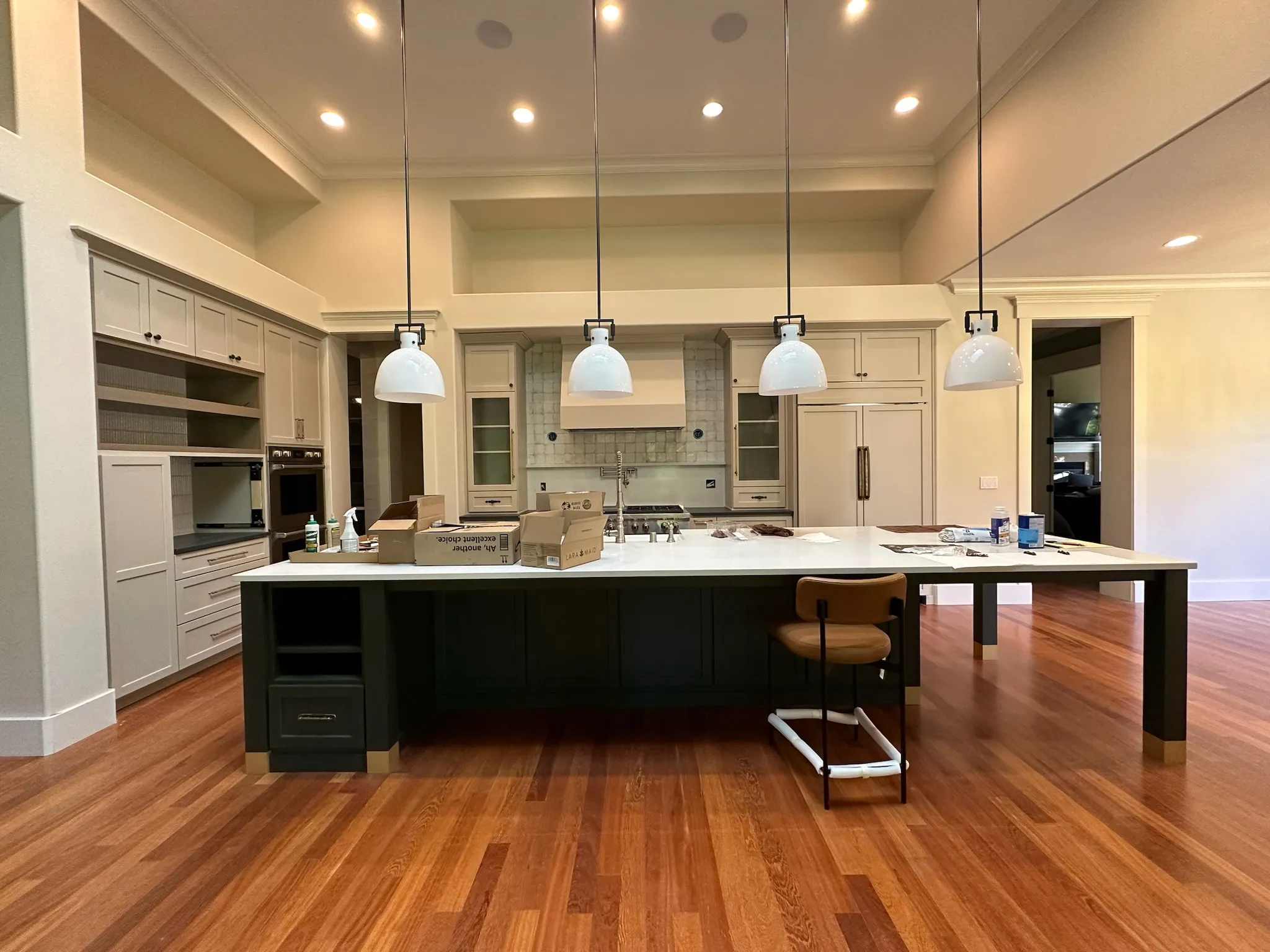 A spacious transitional kitchen featuring a dark green island with white quartz countertop, light neutral cabinetry, and warm hardwood floors. Elegant pendant lights illuminate the space.