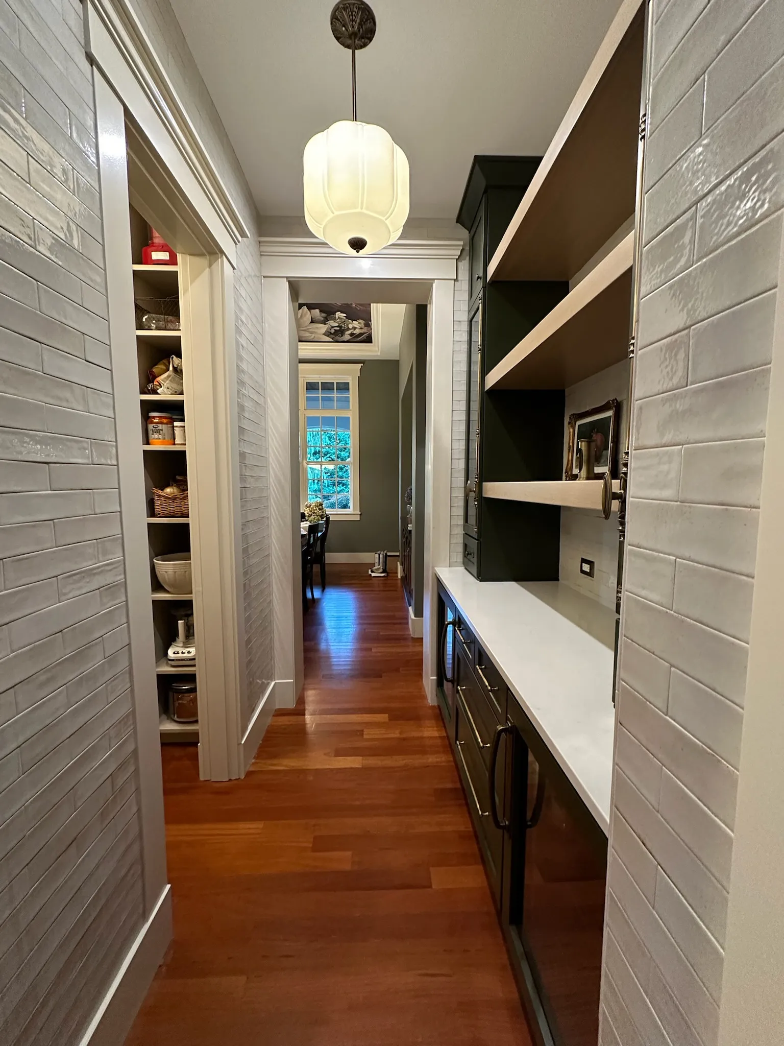 Elegant transitional hallway with dark green custom cabinetry, open wood shelving, white quartz countertop, artisan subway tiles, and a recessed pantry.